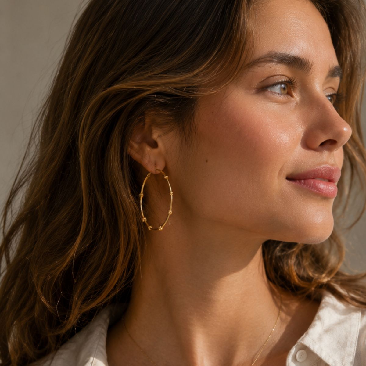 Close-up of a woman wearing gold hoop earrings with a neutral background