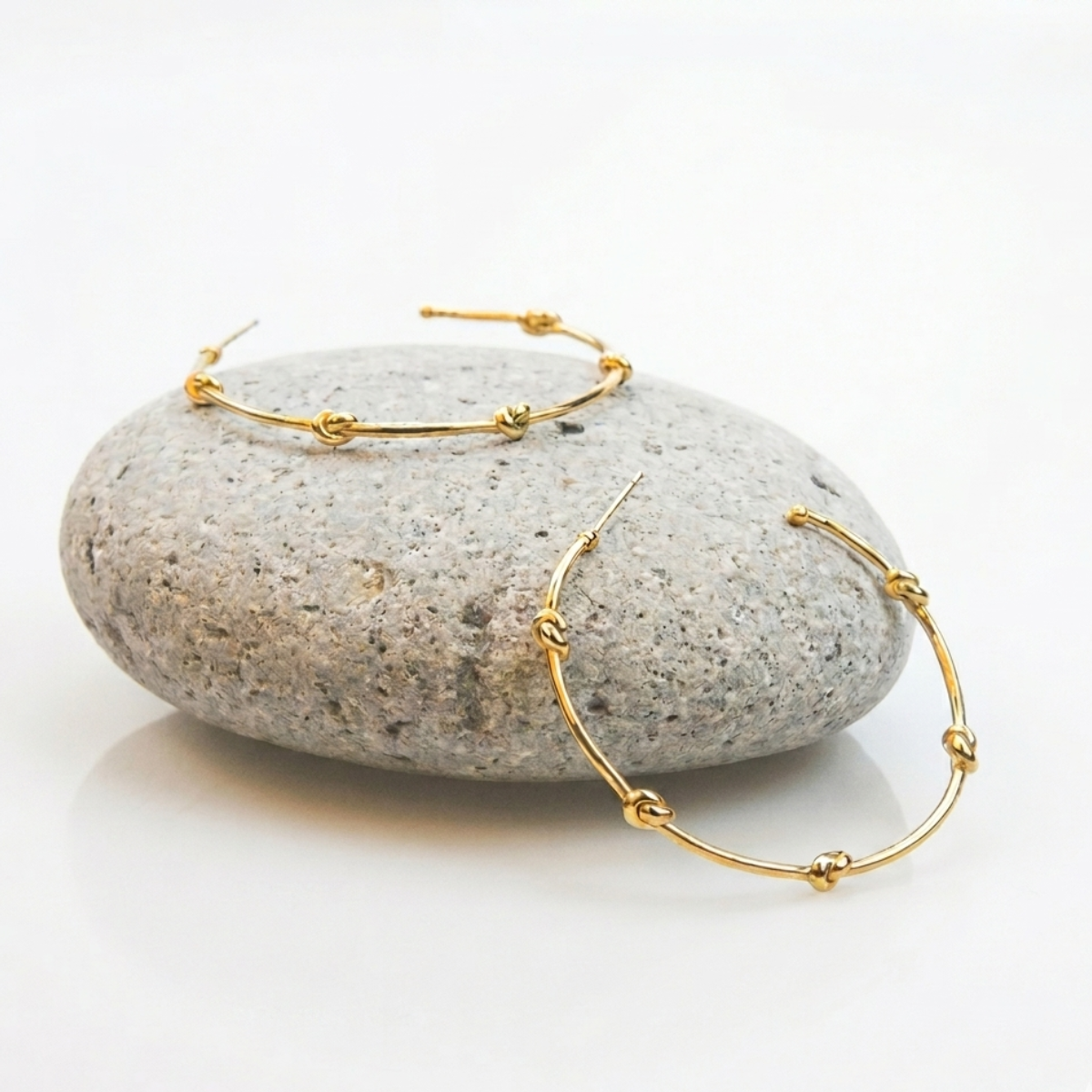 Gold hoop earrings on a gray stone with a white background