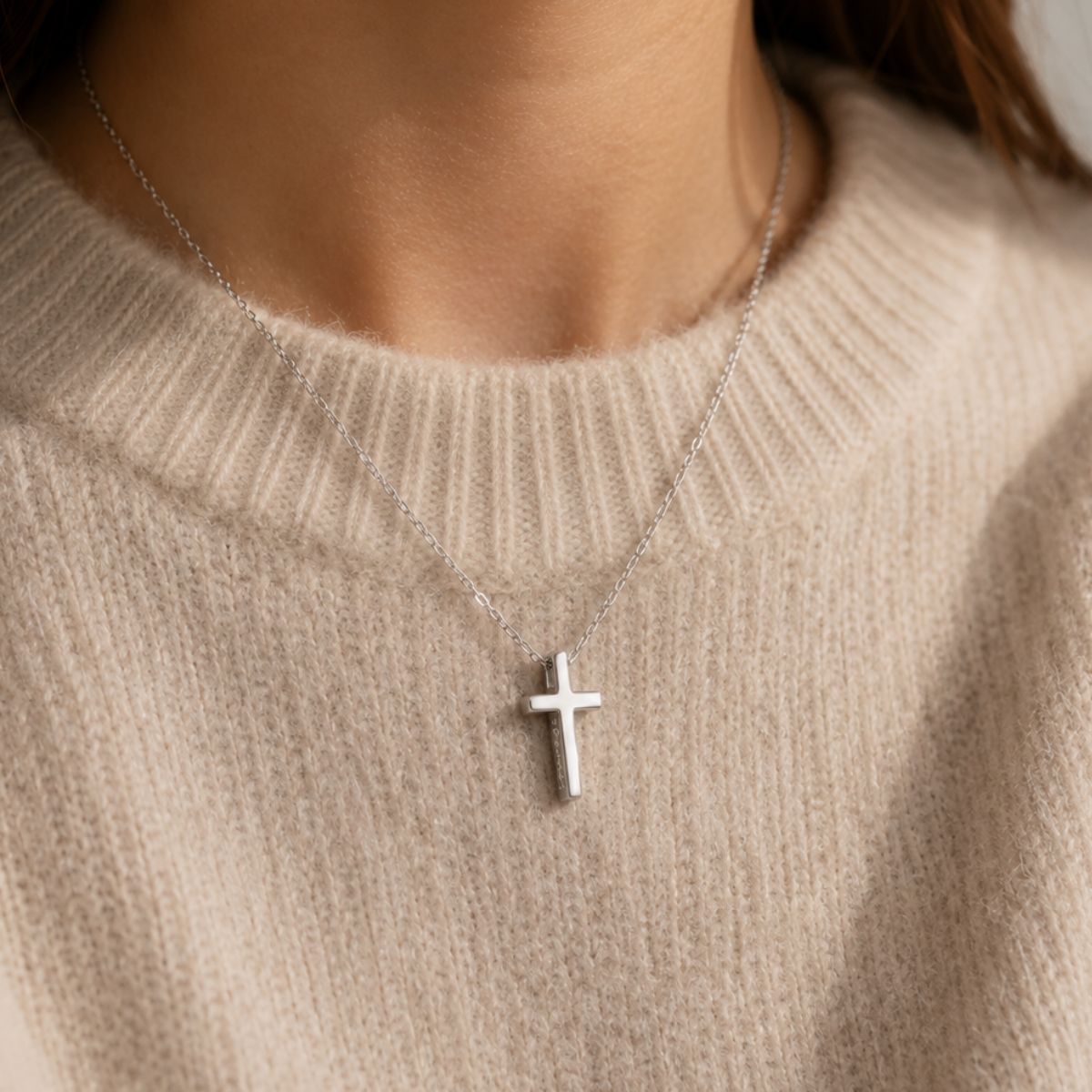 Silver cross necklace on a person wearing a beige sweater