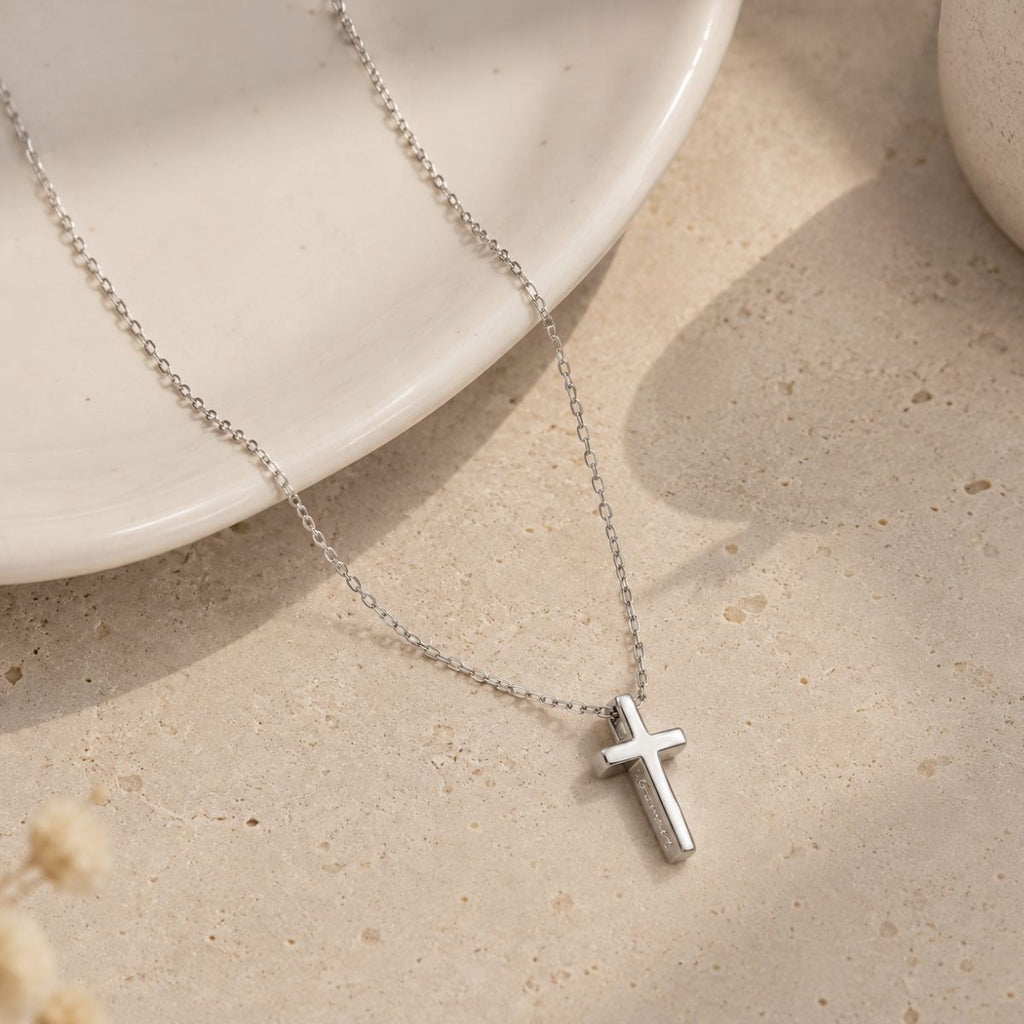 Silver cross necklace on a beige surface with a white dish in the background