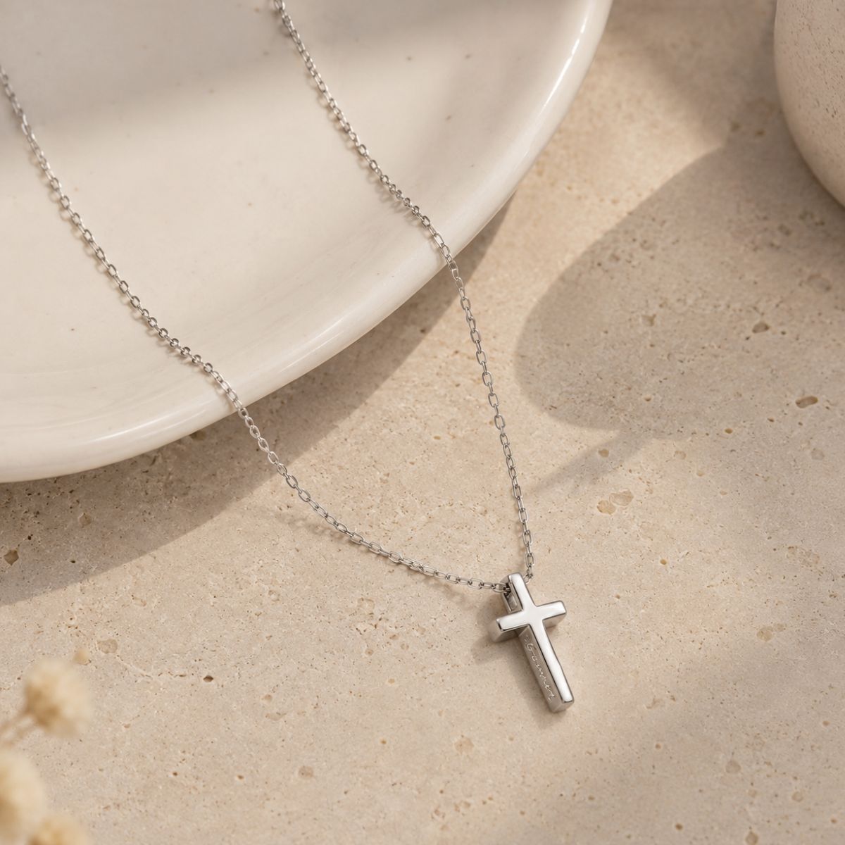 Silver cross necklace on a beige surface with a white dish in the background