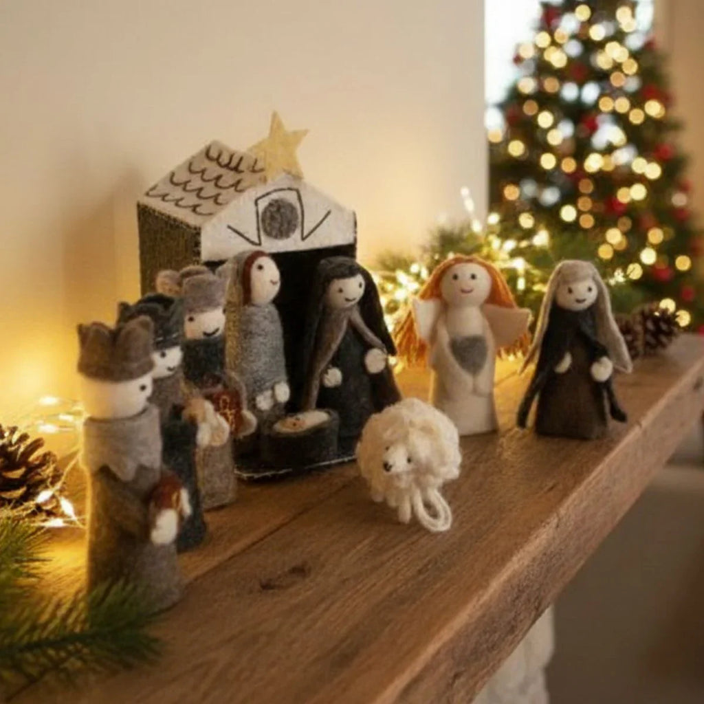 Knitted nativity scene on a wooden surface with a Christmas tree in the background.