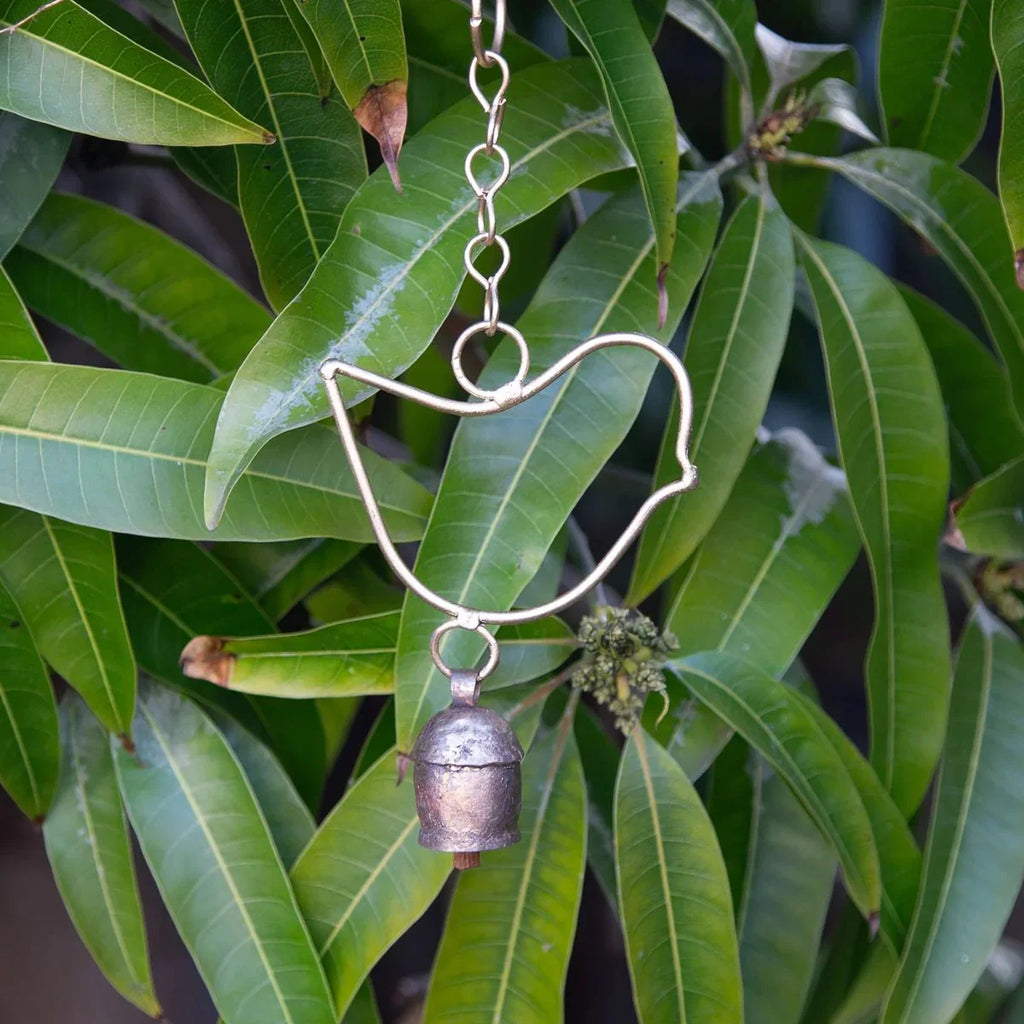 Decorative metal cat-shaped object with a bell hanging among green leaves