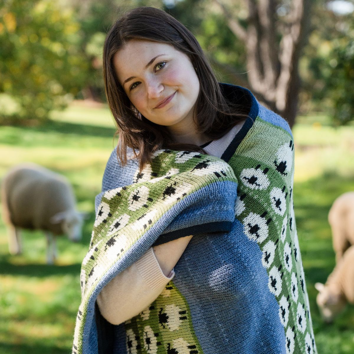 Woman wearing a green and blue patterned shawl in a pastoral setting with sheep.