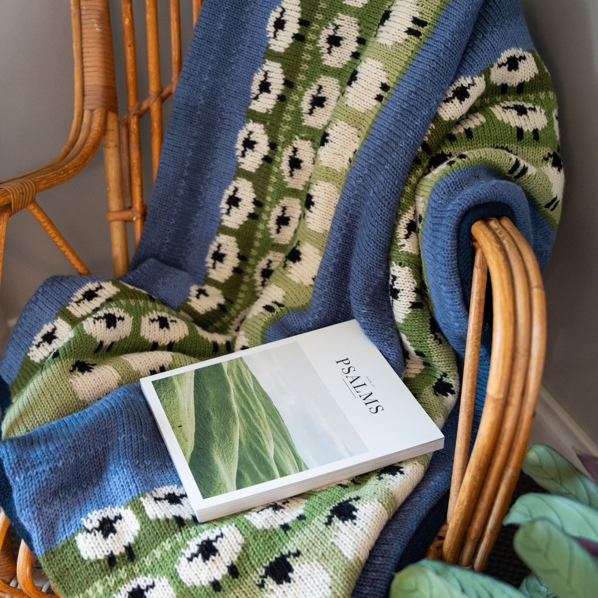 Knitted blanket with floral pattern draped over a chair, featuring a book titled 'Psalms'.