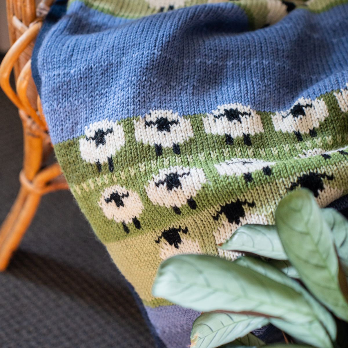 Knitted blanket with sheep pattern draped over a chair