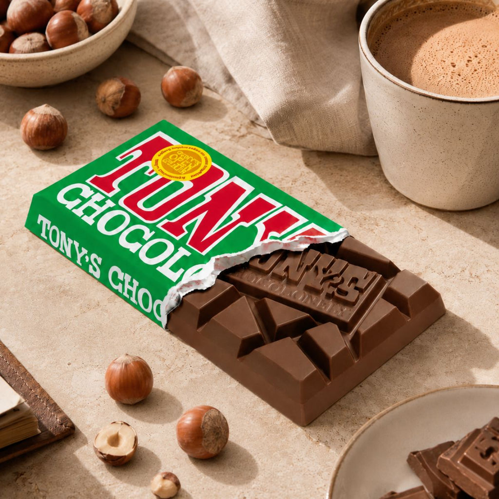 Chocolate bar with Tony's Chocolonely packaging on a table with hazelnuts and coffee.