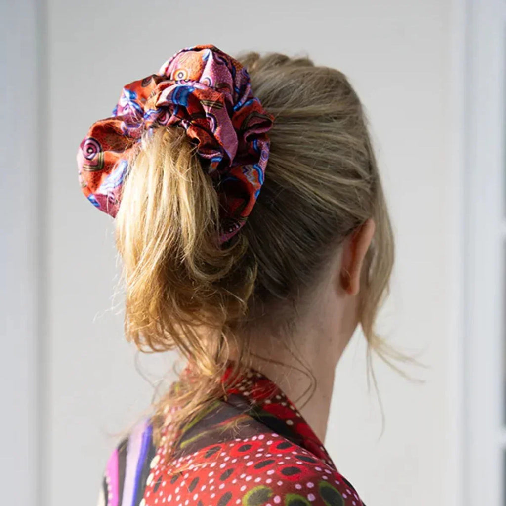 Person wearing a colorful patterned scrunchie in their hair against a white background