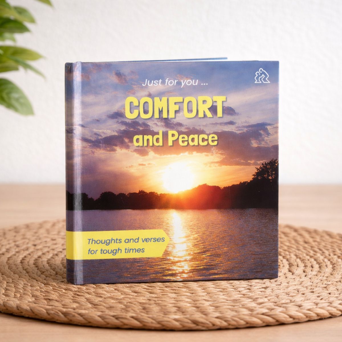 Book titled 'Comfort and Peace' with a sunset over water cover on a woven surface.
