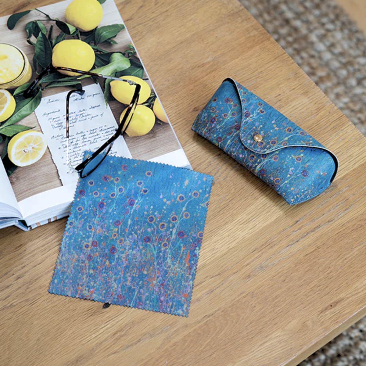 Floral-patterned sunglasses case on a wooden surface with a book and lemons.