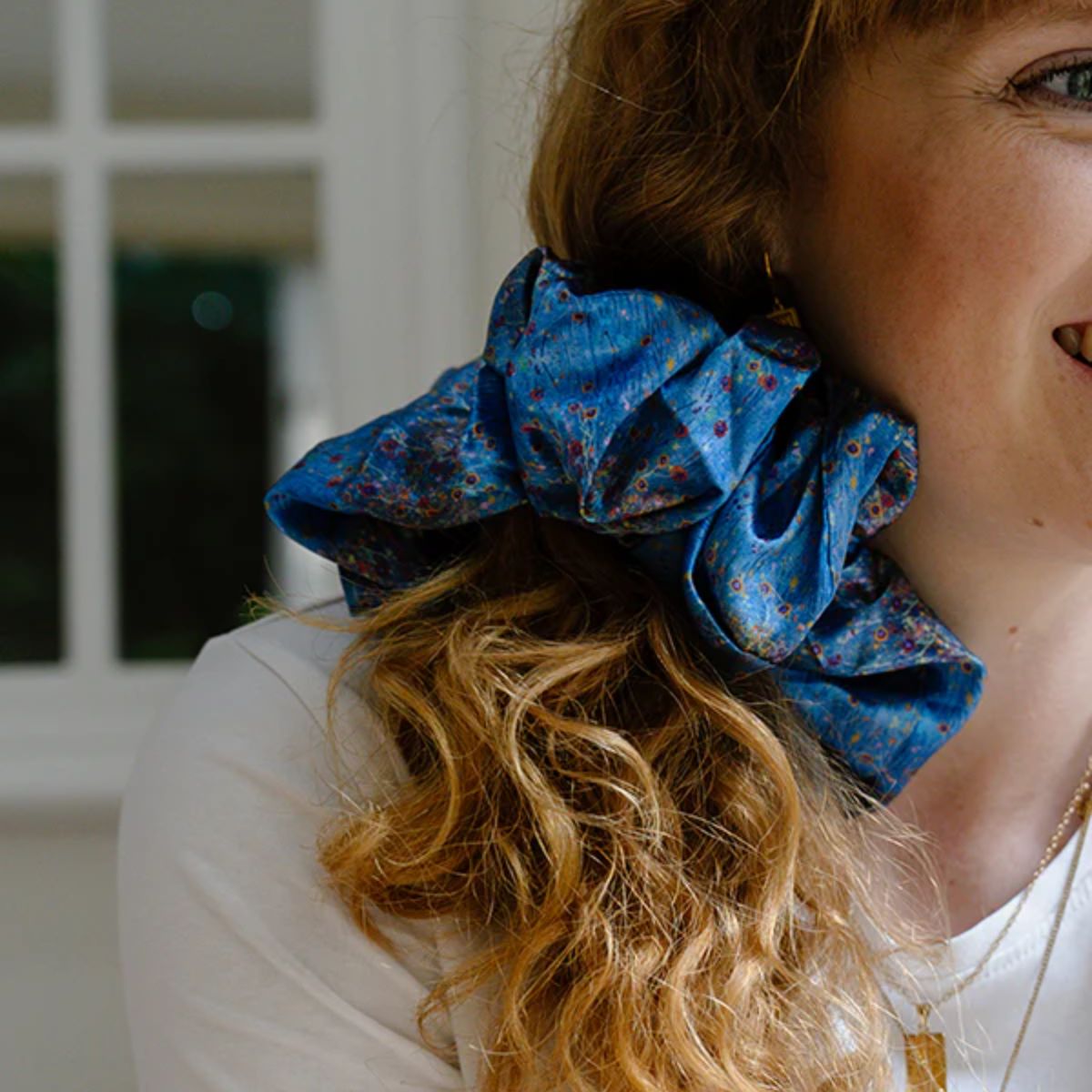 Person wearing a blue floral scrunchie in their hair with a blurred background