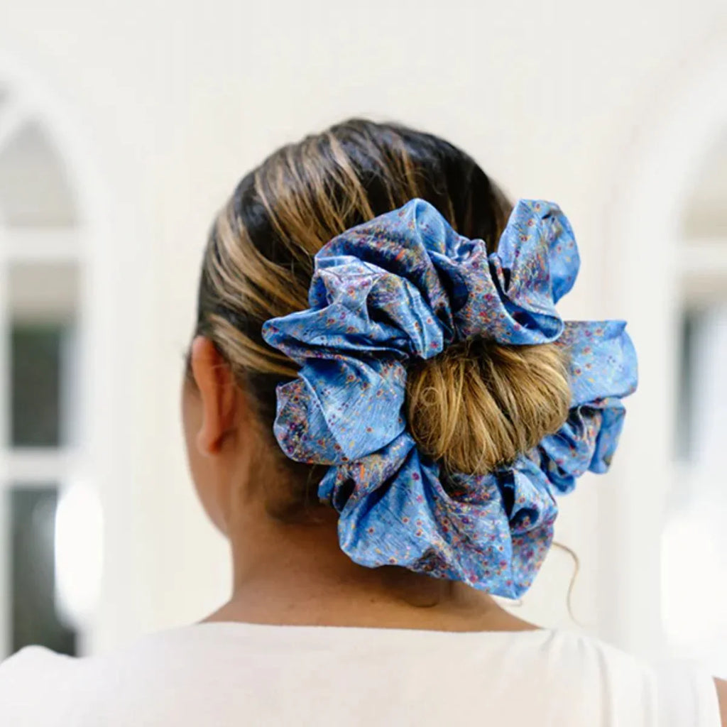 Person wearing a blue floral scrunchie in their hair with a blurred background