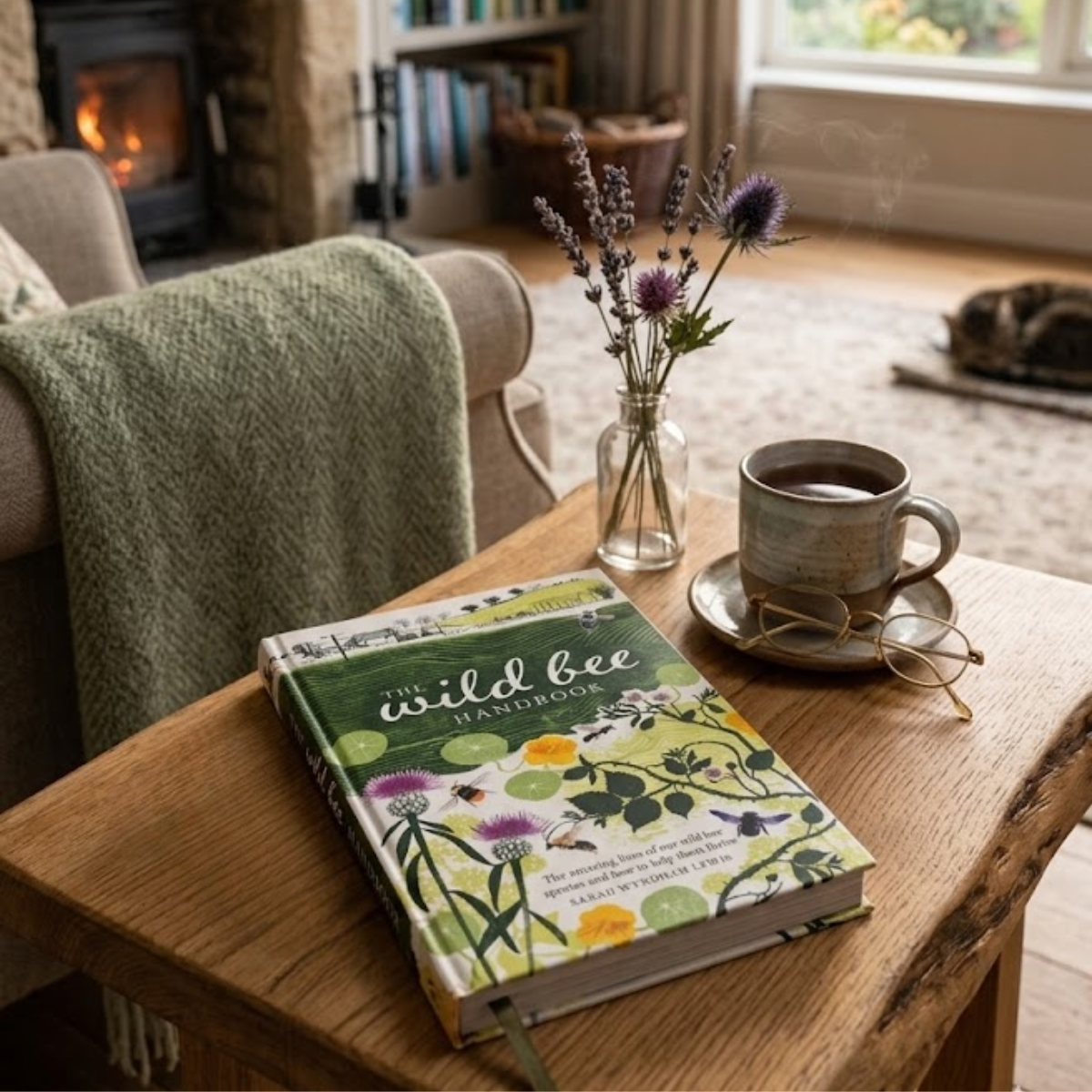 The wild bee handbook on a wooden table next to a cup of tea and glasses in a living room. 