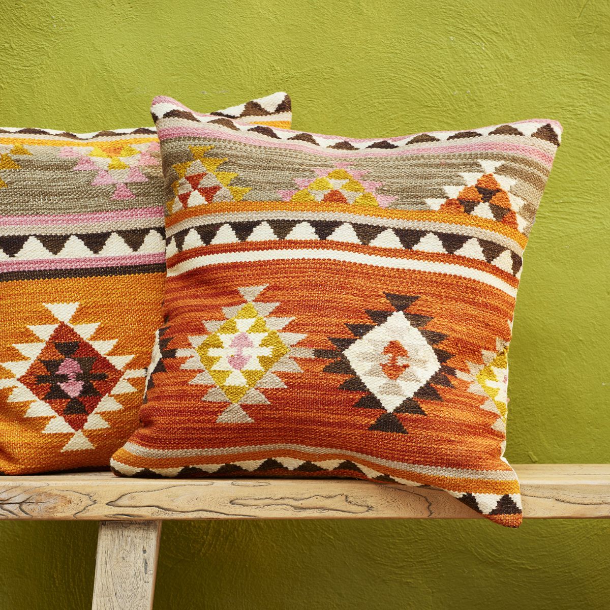Two patterned pillows on a wooden surface against a green wall