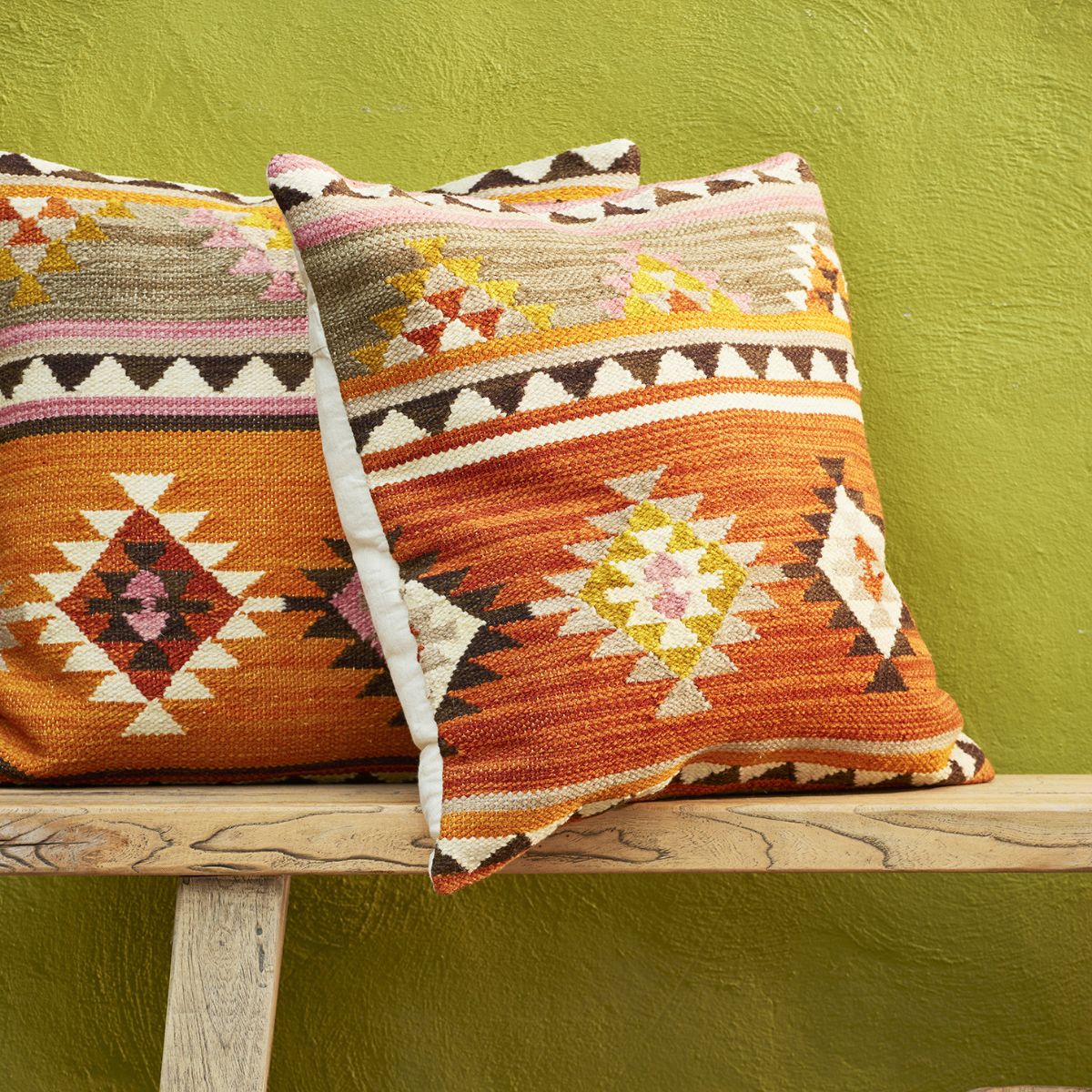 Two patterned pillows on a wooden bench against a green wall