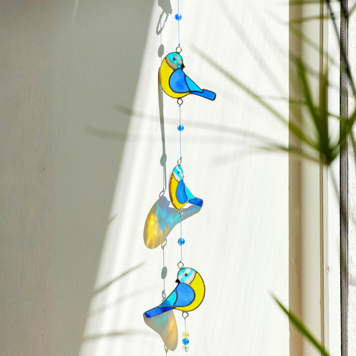 Decorative hanging mobile with colorful bird designs in front of a window.