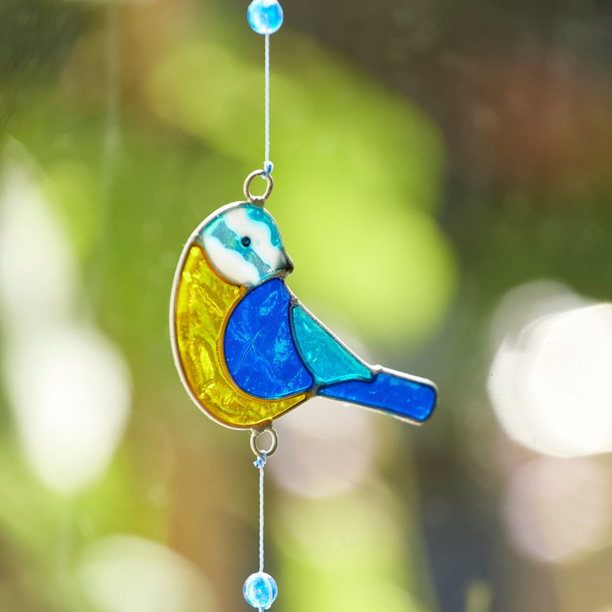 Stained glass bird ornament with blue and yellow colors against a blurred natural background