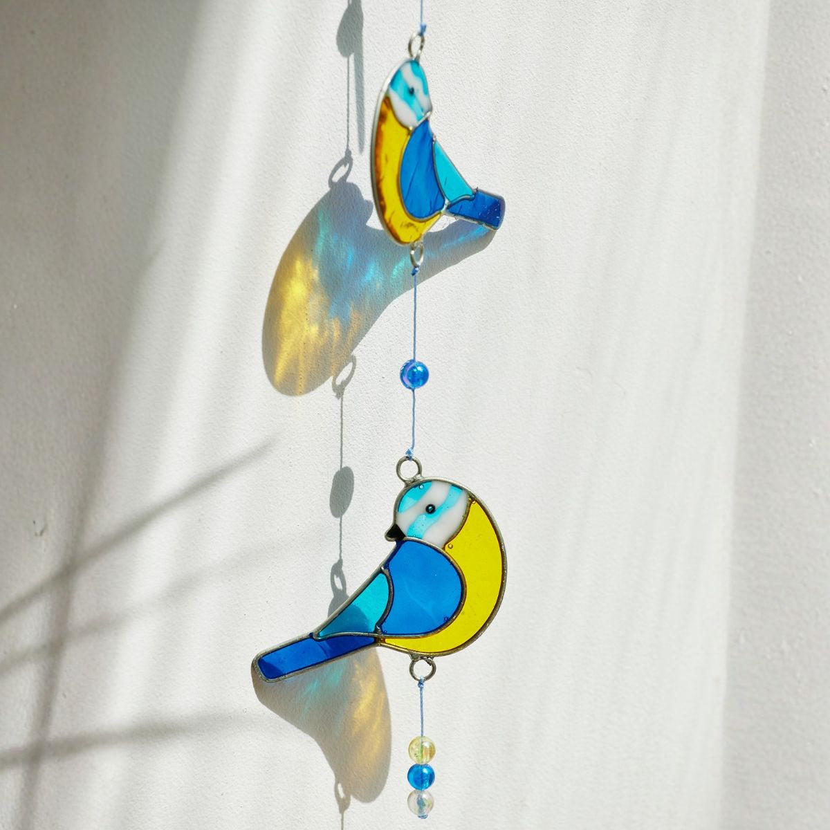 Stained glass bird suncatcher with blue and yellow colors on a white background