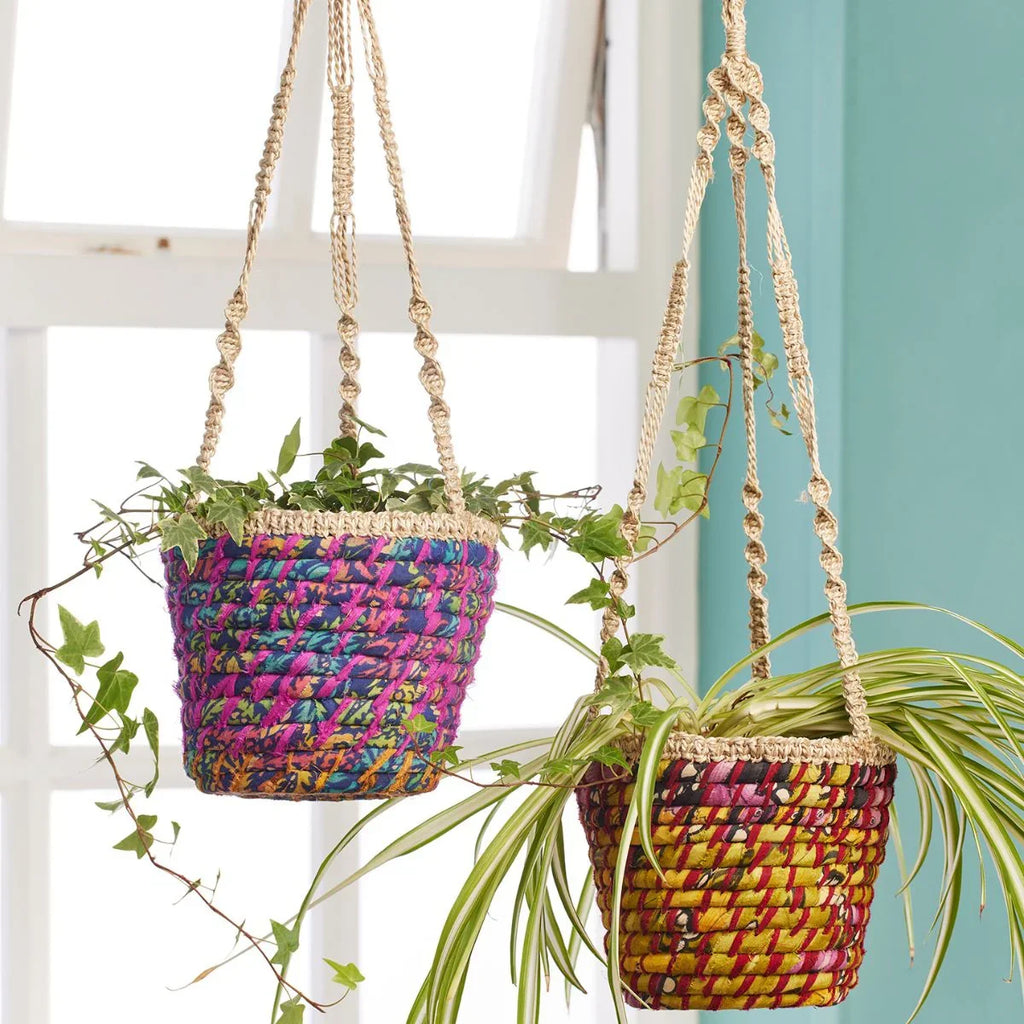 Two colorful woven plant hangers with plants against a light blue wall.