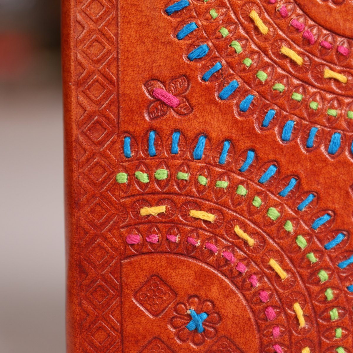 Close-up of a brown leather journal cover featuring intricate hand-tooled geometric patterns and colorful embroidered details in blue, pink, yellow, and green.