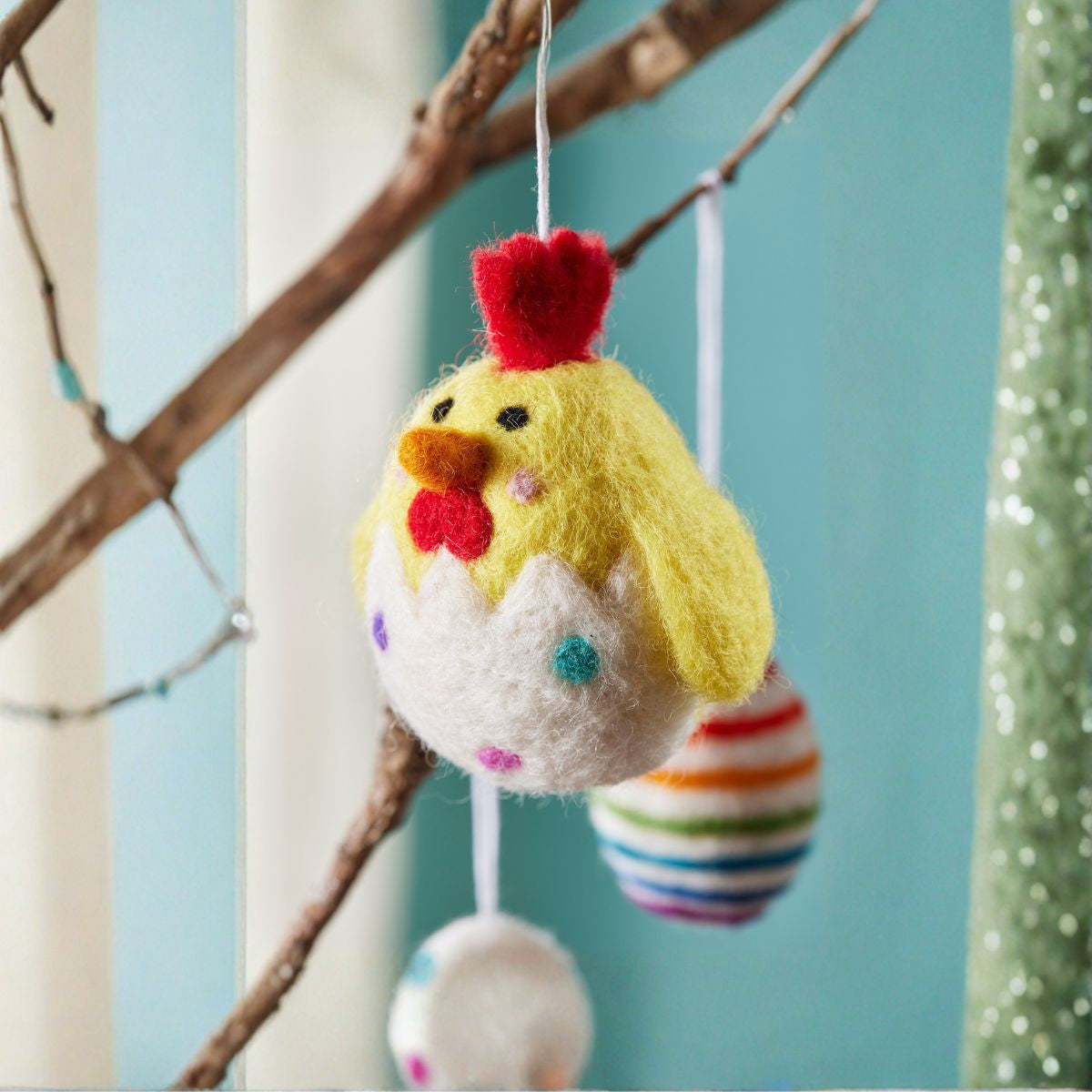 Colorful felt chicken ornament hanging from a branch with a blue background