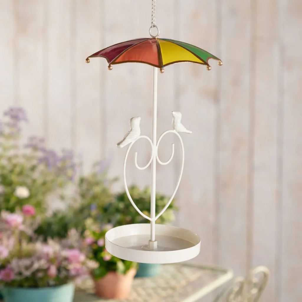 Decorative hanging bird feeder with a colorful umbrella and birds on a blurred garden background