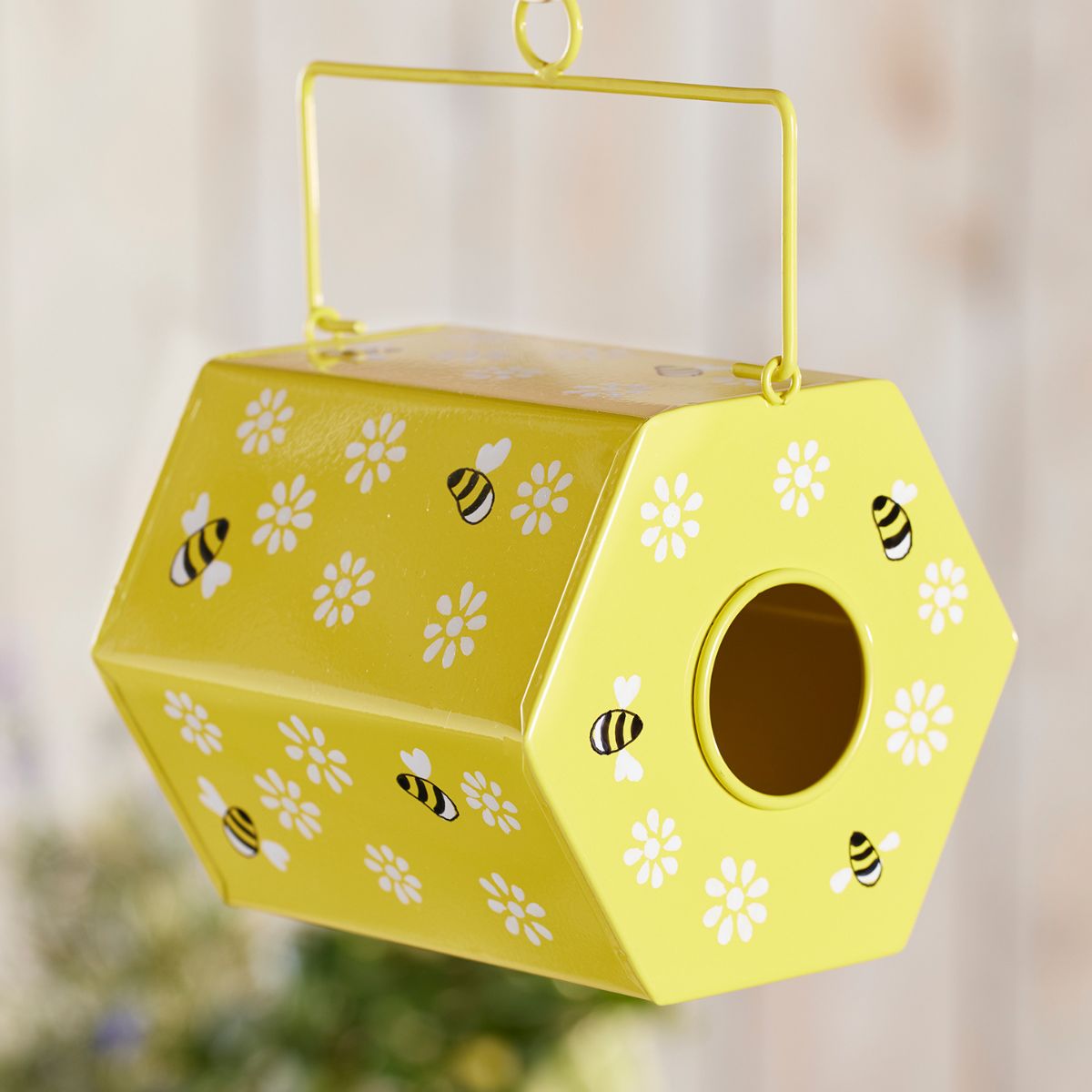Yellow bee and flower patterned birdhouse hanging against a blurred natural background