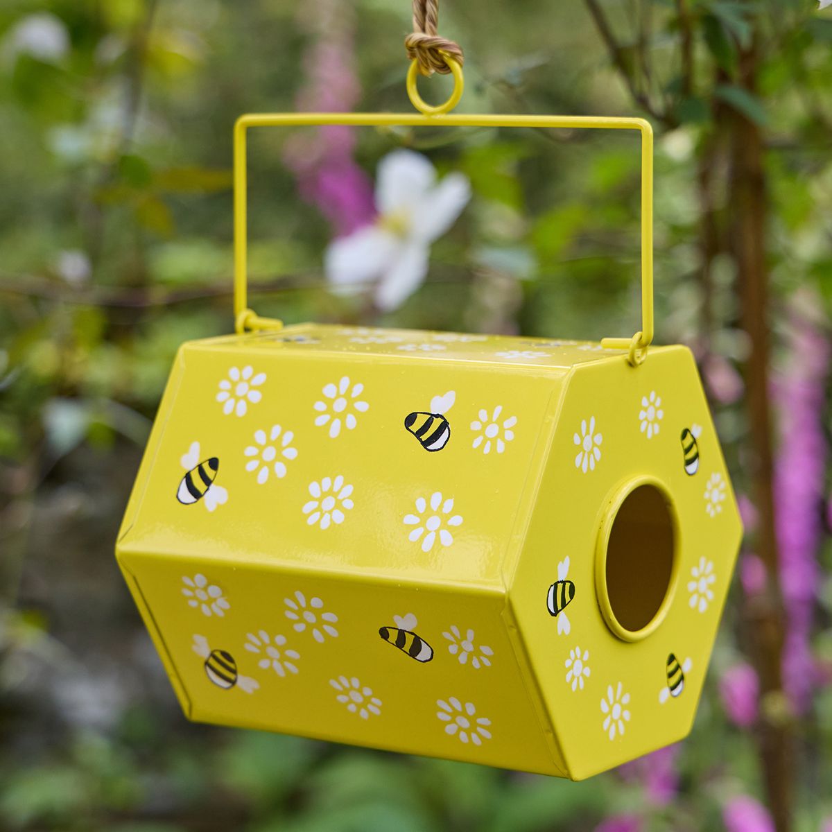 Yellow bee house with floral and bee patterns hanging against a blurred natural background.