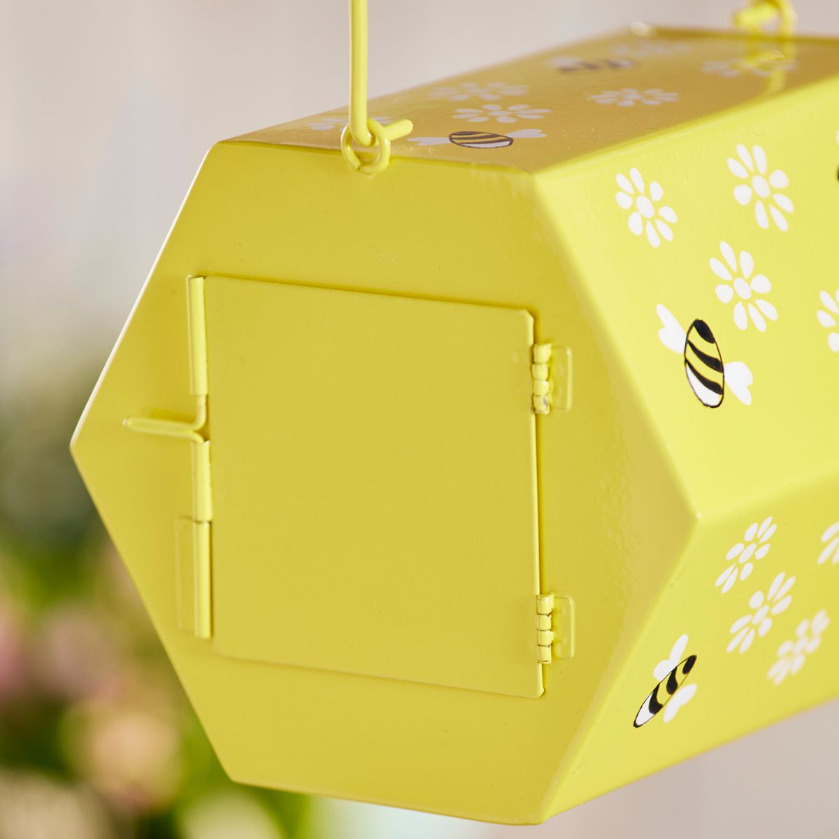 Yellow bee-themed box with floral patterns on a blurred natural background