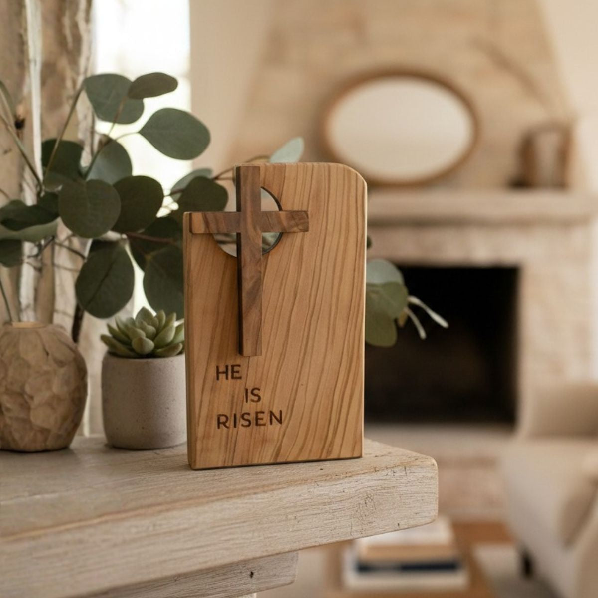 Wooden cross with 'He is Risen' engraving on a wooden surface with plants in the background