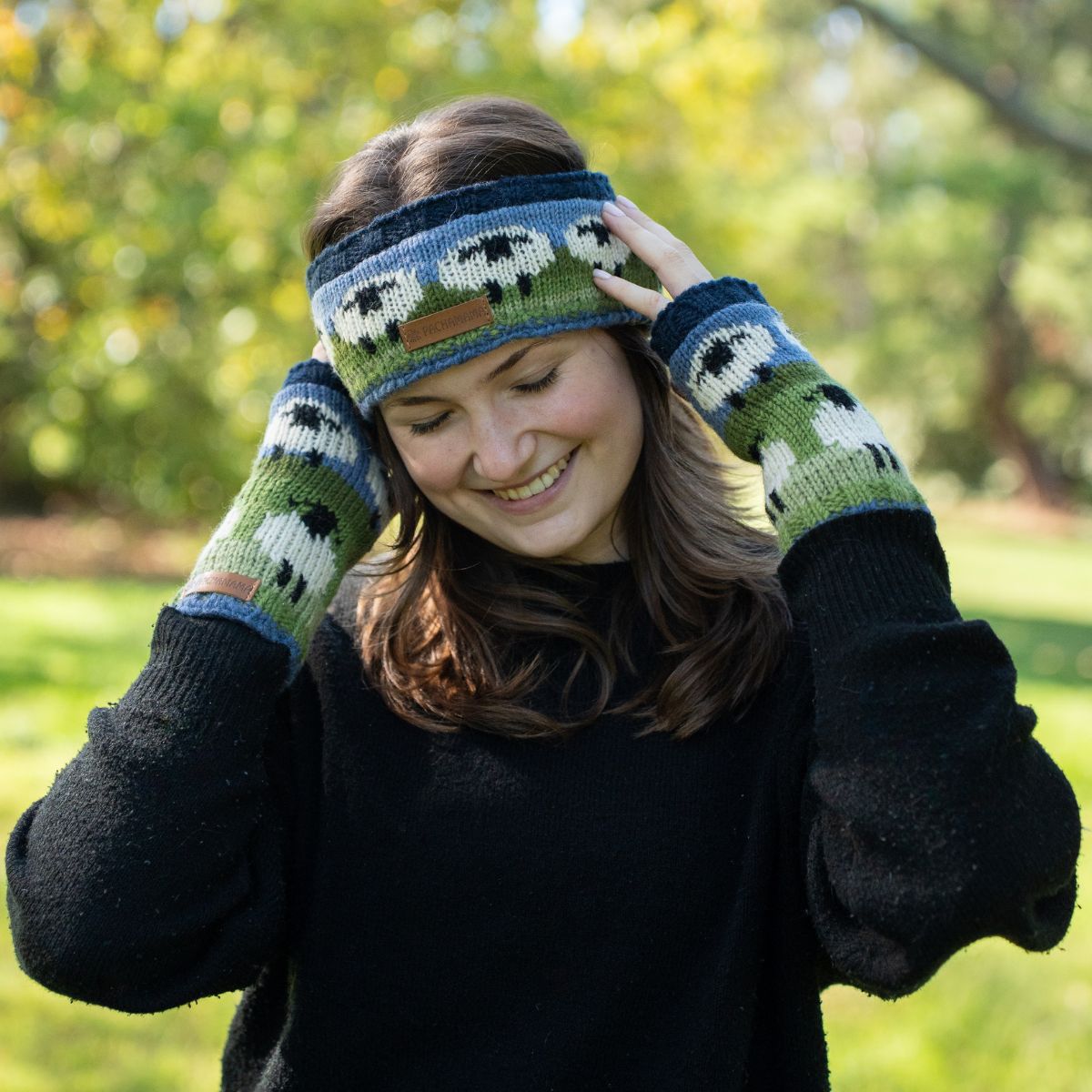 Person wearing a black sweater and green knitted hat with sheep pattern outdoors