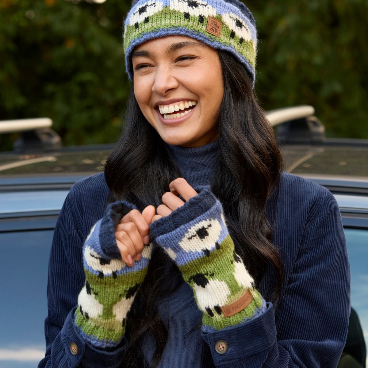 Person wearing a matching knit hat and mittens with sheep pattern, sitting outdoors.