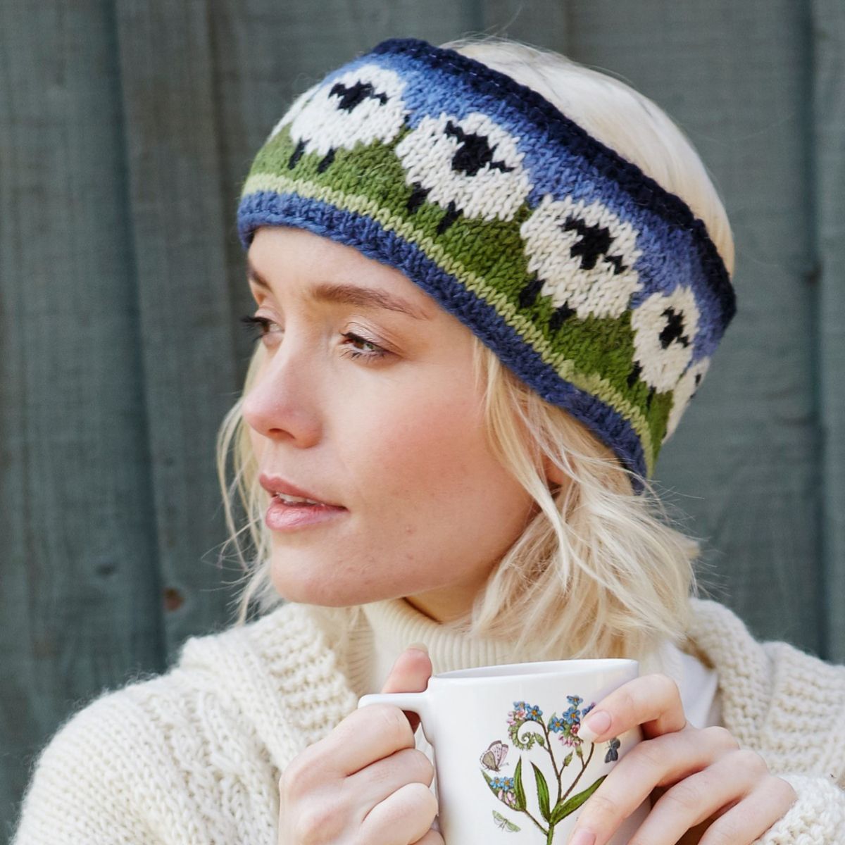 Woman wearing a knitted headband with floral pattern, holding a mug.