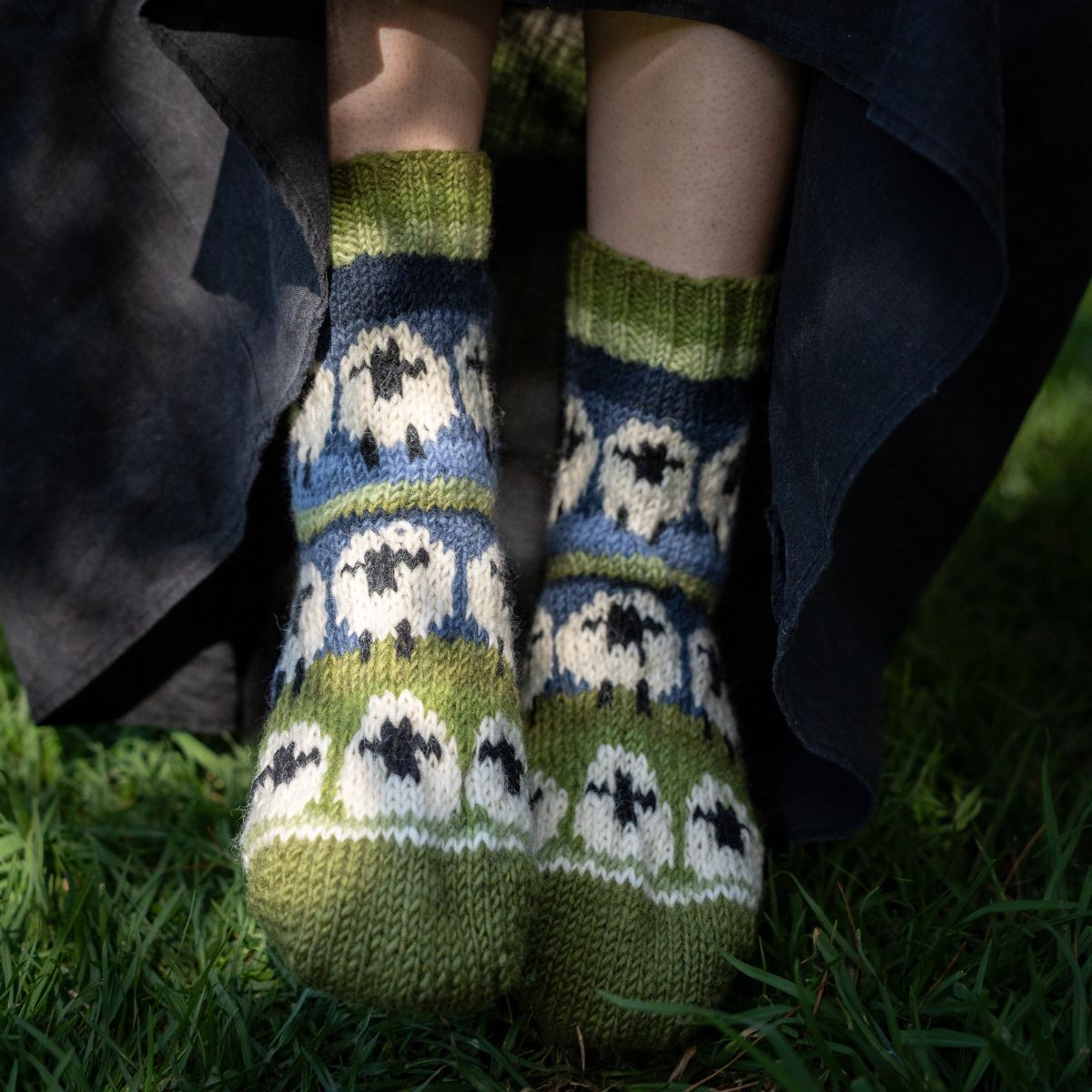 Knitted socks with a sheep pattern worn outdoors on grass