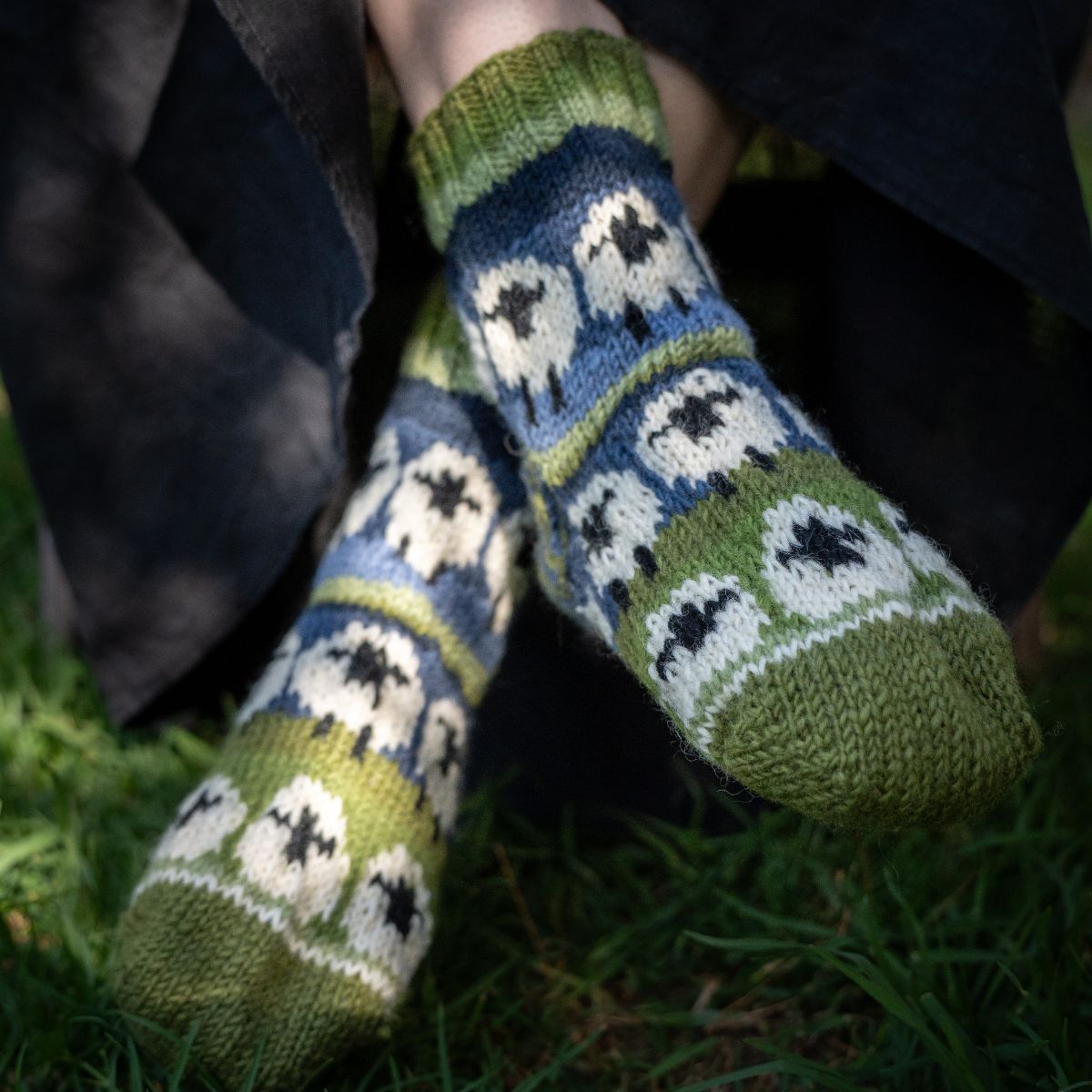 Knitted socks with sheep pattern worn by a person sitting on grass