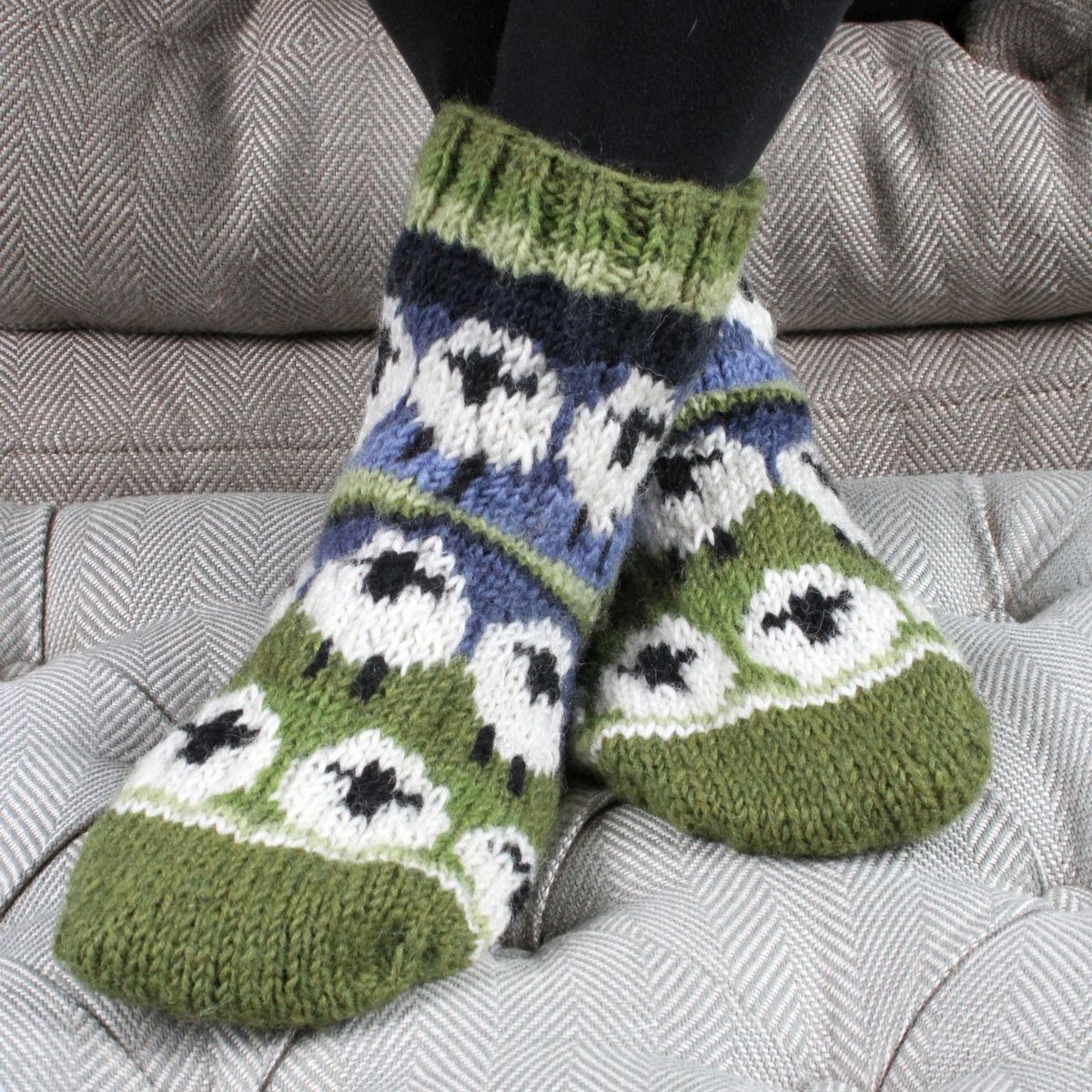 Knitted socks with a pattern of black, white, and blue on a gray couch.