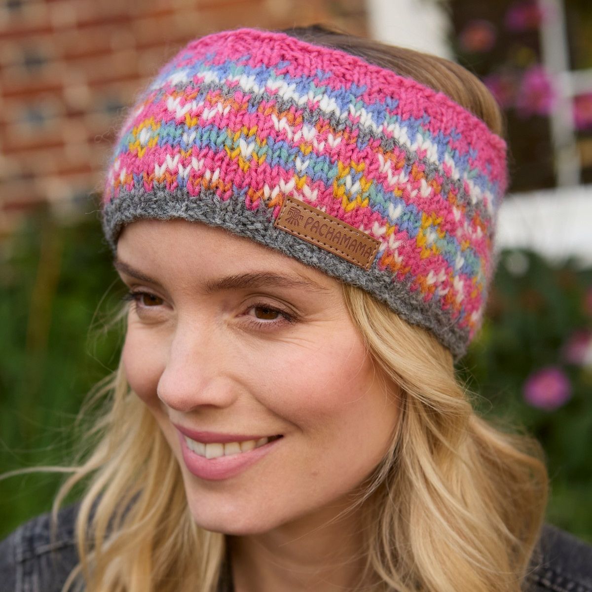 Woman wearing a colorful knitted headband with a brand logo, outdoors.