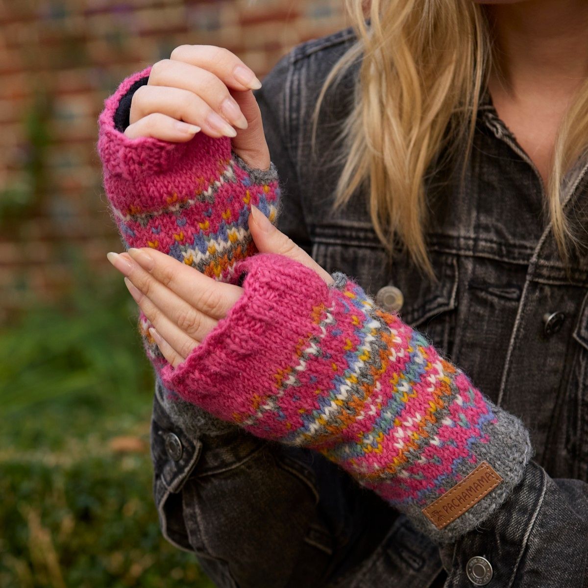 Person wearing colorful knitted fingerless gloves with a blurred outdoor background