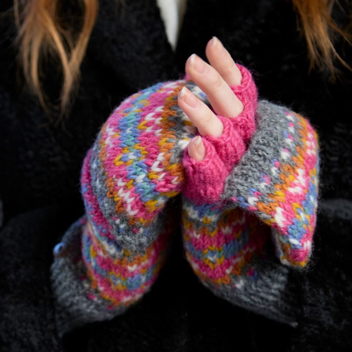Colorful knitted fingerless gloves with a pink cuff on a dark background