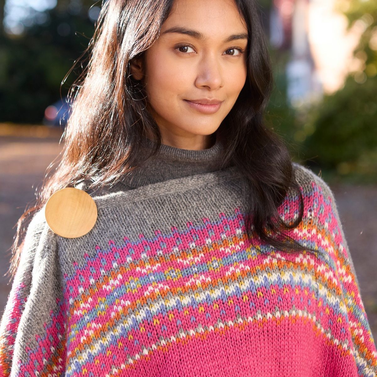 Woman wearing a colorful knitted poncho with a blurred outdoor background