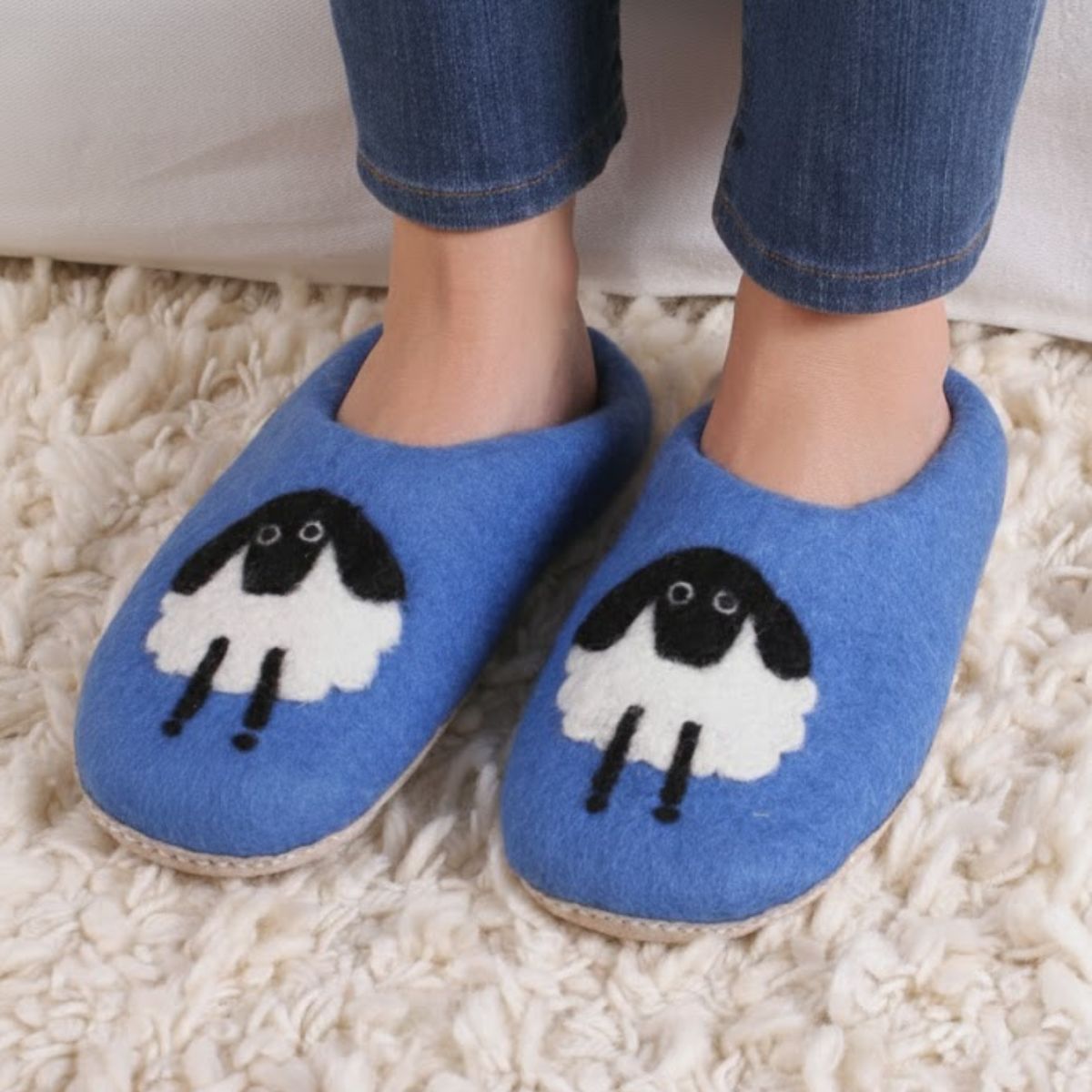 Blue slippers with sheep design worn on a fluffy white carpet