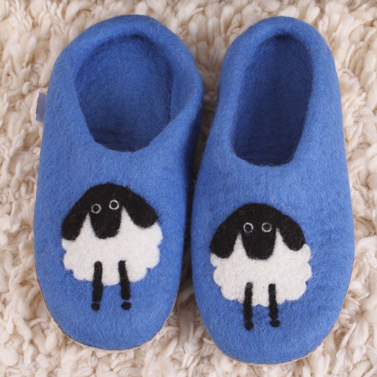 Pair of blue slippers with sheep design on a textured surface