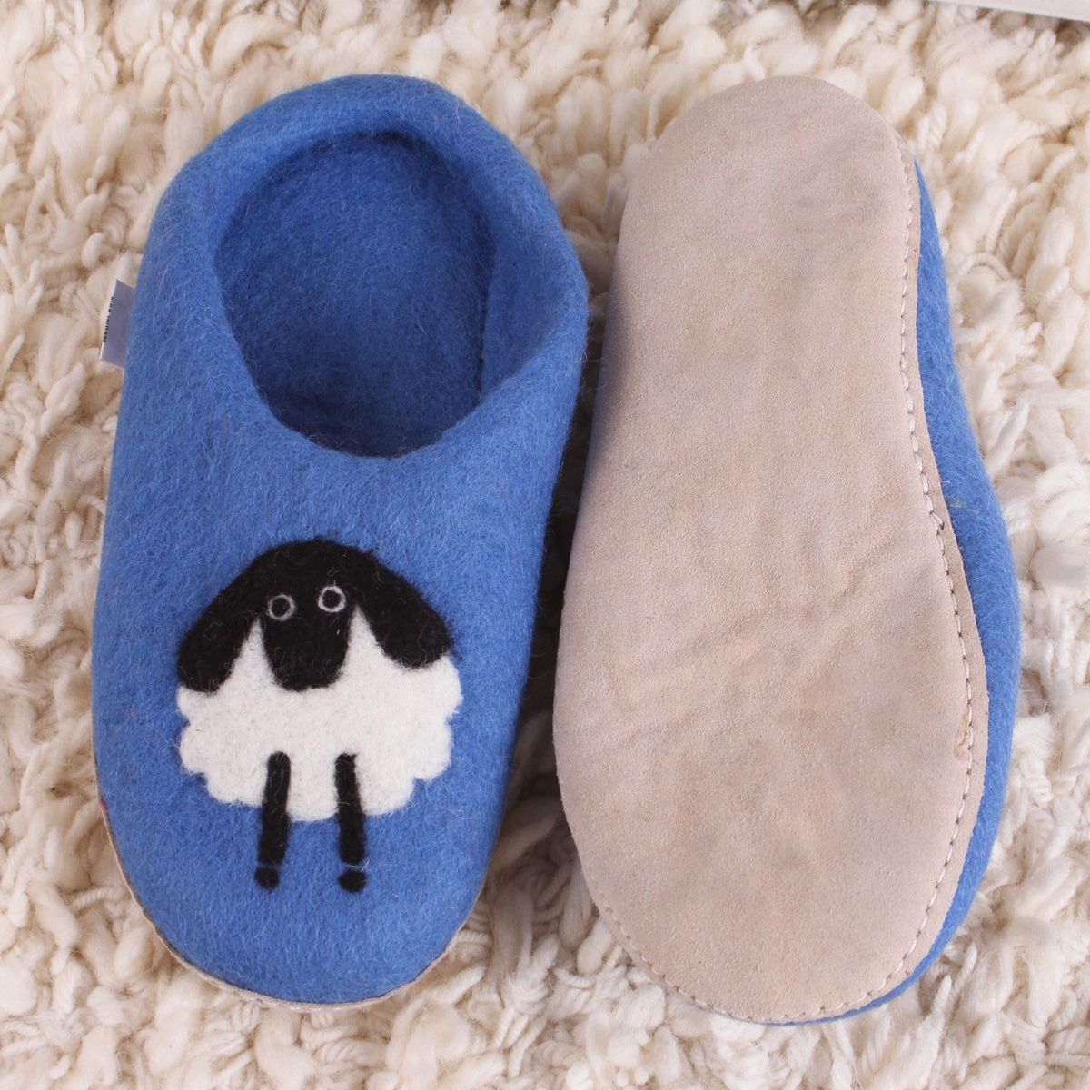 Pair of blue slippers with a sheep design on a textured surface