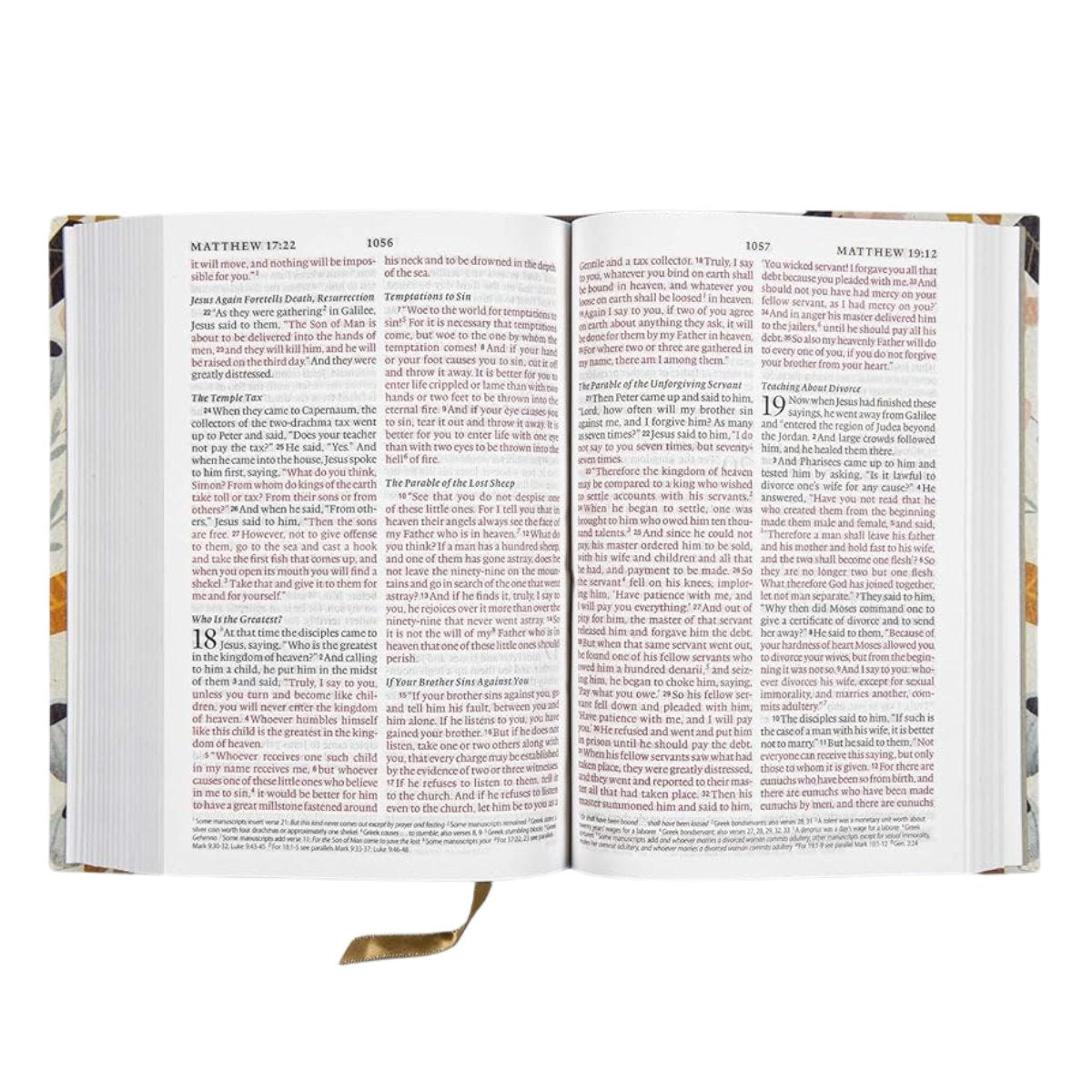 An open Bible showing two spread pages with printed text, photographed against a plain white background. The book has a decorative multicolor floral pattern on the cover and a gold ribbon bookmark hanging from the bottom margin.