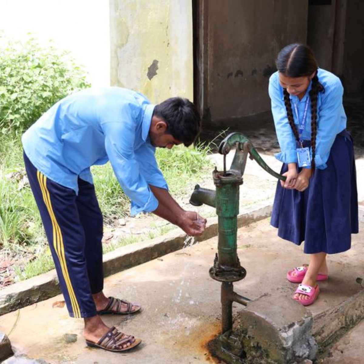 Two people using a manual water pump outdoors.