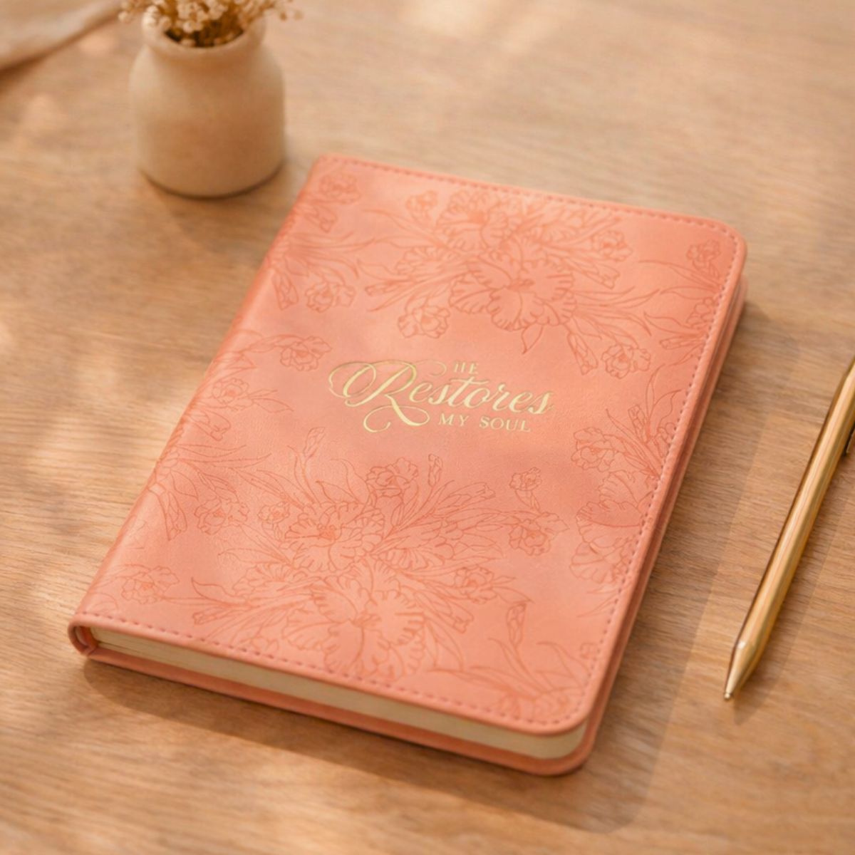 Pink notebook with floral embossing and a pen on a wooden surface