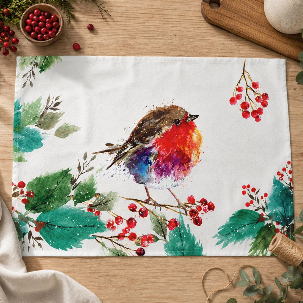 A rectangle white tea towel with a colorful watercolor robin bird and red berries printed on it, styled on a wooden tabletop with small decorative props.