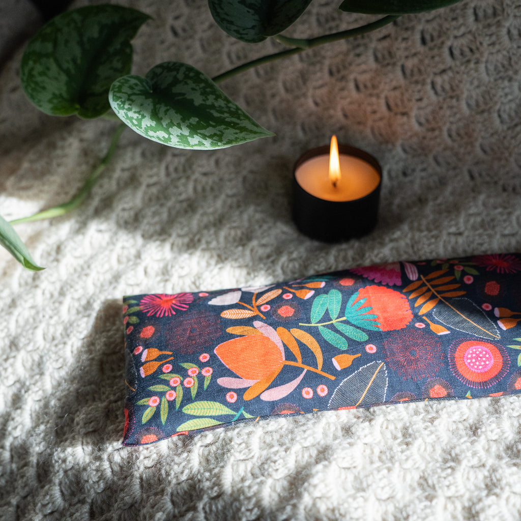 Patterned navy heat bag on a wool blanket next to a candle and ivy 