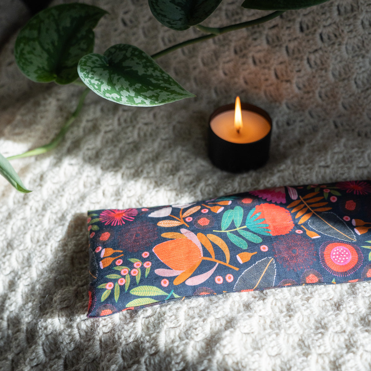 Patterned navy heat bag on a wool blanket next to a candle and ivy 