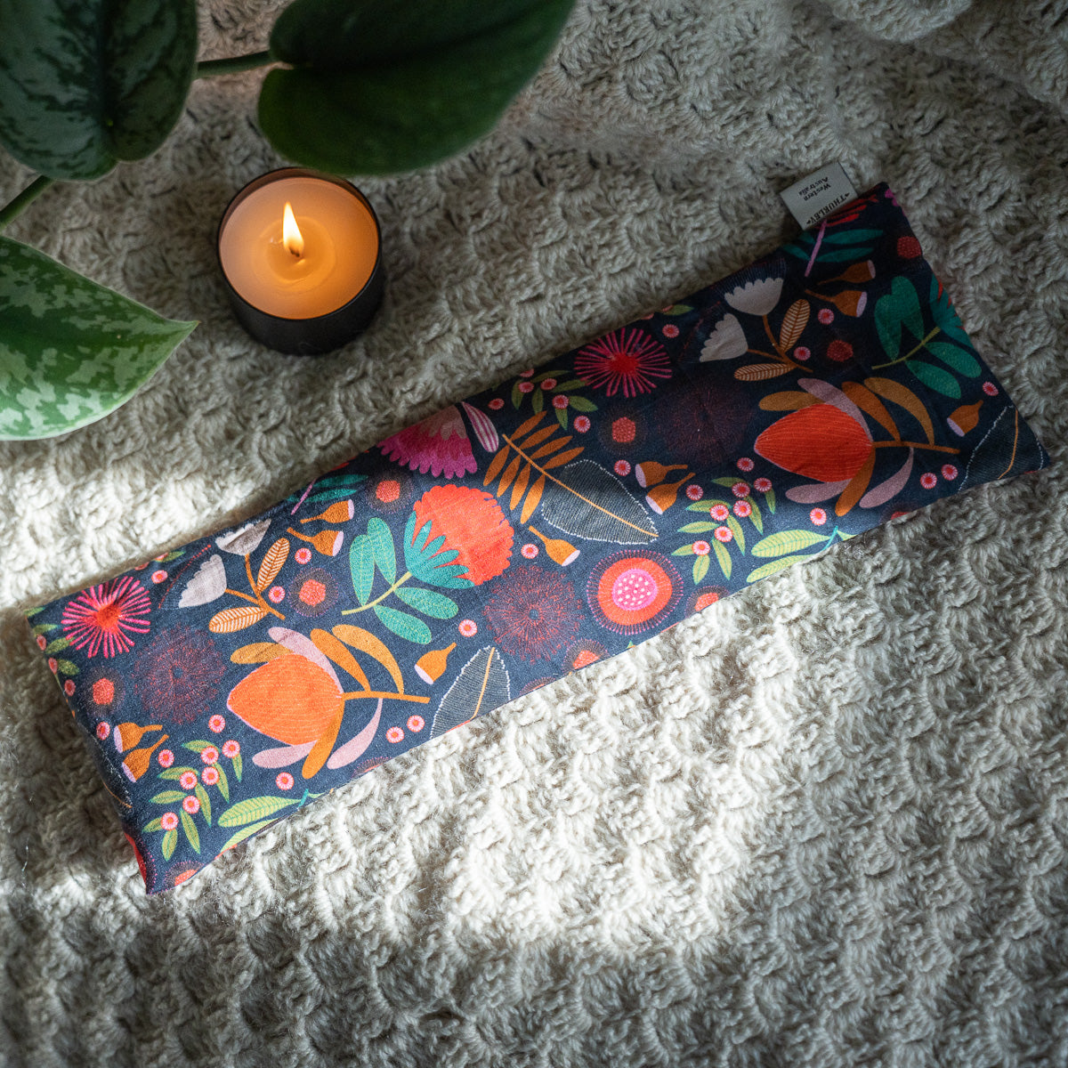 Patterned navy heat bag on a wool blanket next to a candle and ivy 
